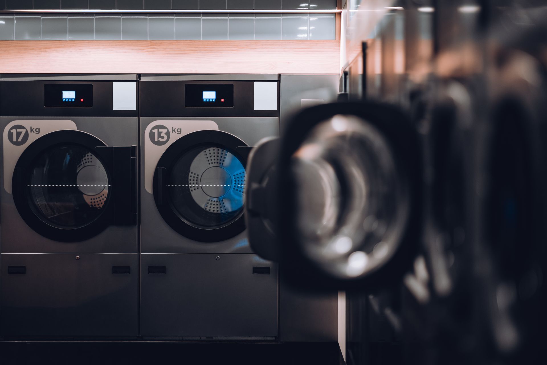 Machines à laver dans une laverie automatique faiblement éclairée, une porte ouverte laissant apparaître un intérieur bleu.