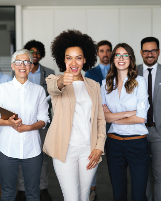 Group of diverse professionals smiling, with woman in center giving thumbs-up, wearing beige blazer and white pants.