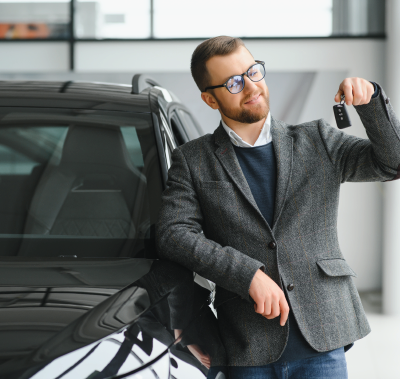 A man in a suit is holding a car key in front of a car.