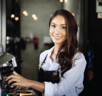 A woman wearing an apron is standing in front of a coffee machine.