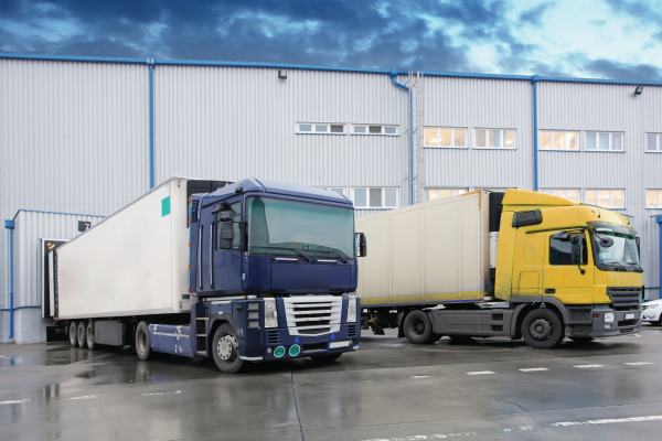 Two semi trucks are parked in front of a warehouse.