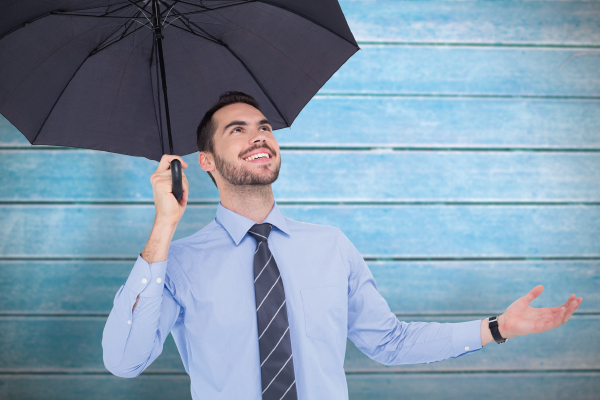 A man in a blue shirt and tie is holding an umbrella over his head.