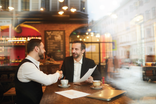 Two men are shaking hands while sitting at a table in a restaurant.