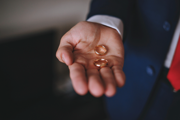 A man in a suit and tie is holding a pair of wedding rings in his hand.