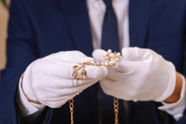 A man in a suit and white gloves is holding a gold necklace.