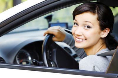 A woman is smiling while driving a car and looking out the window.