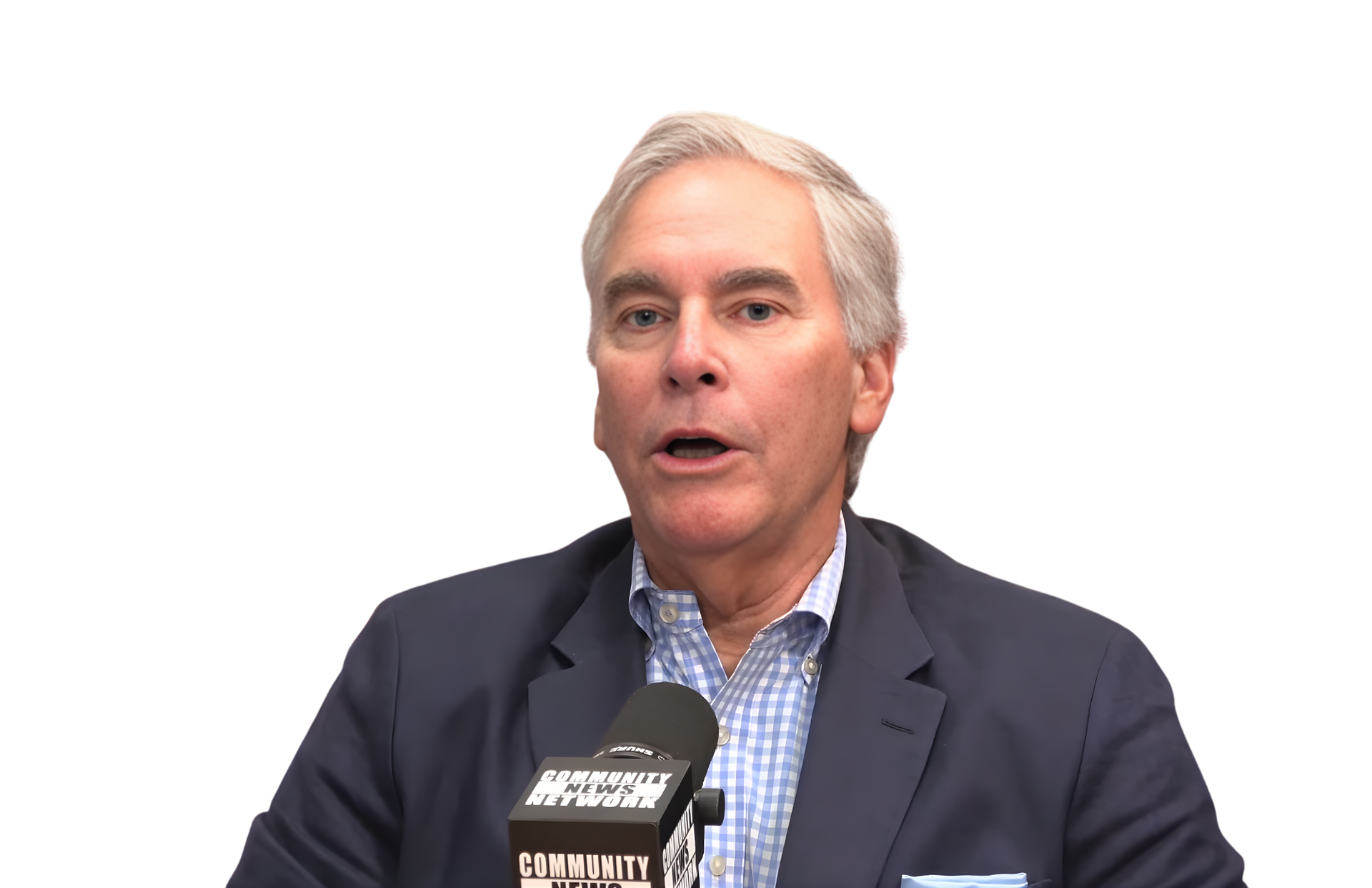 Man speaking into a microphone, wearing a blazer over a blue and white patterned shirt.