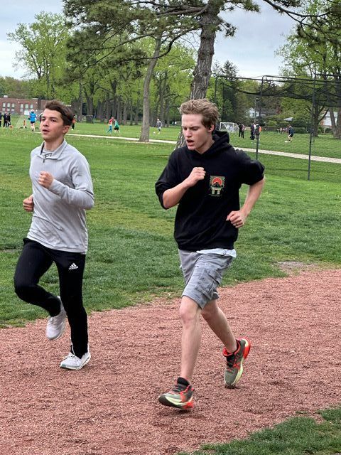 Two people running on a dirt track in a park. One in black pants, the other in shorts.