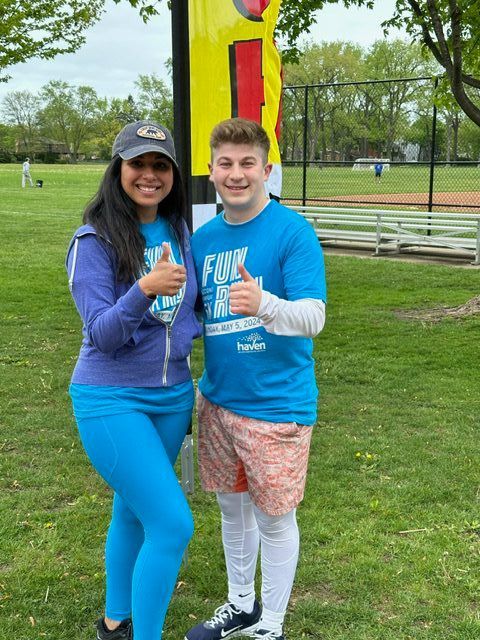 Two people giving thumbs up at an outdoor event, one in blue leggings, other in swim trunks.