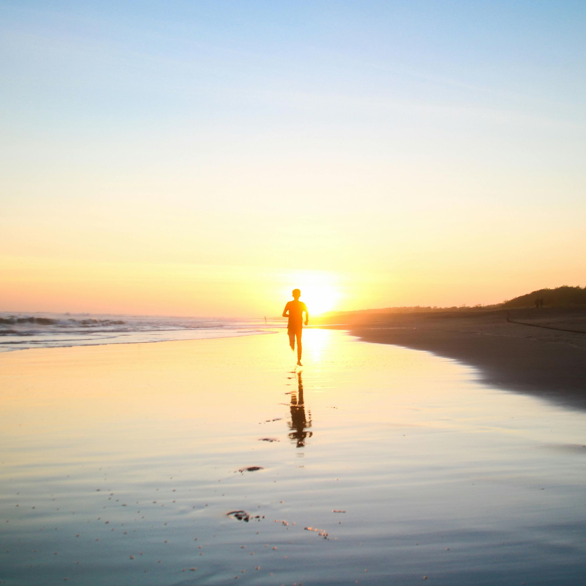 Person running on a wet beach at sunset, with golden light reflecting in the water.