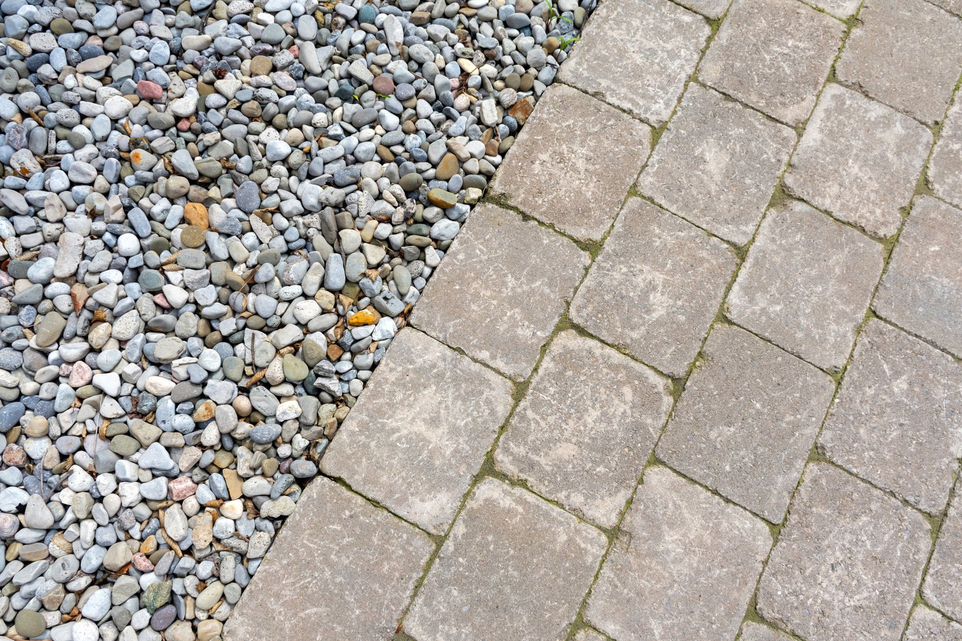 Gravel and light brown square paving stones meeting at an angle.