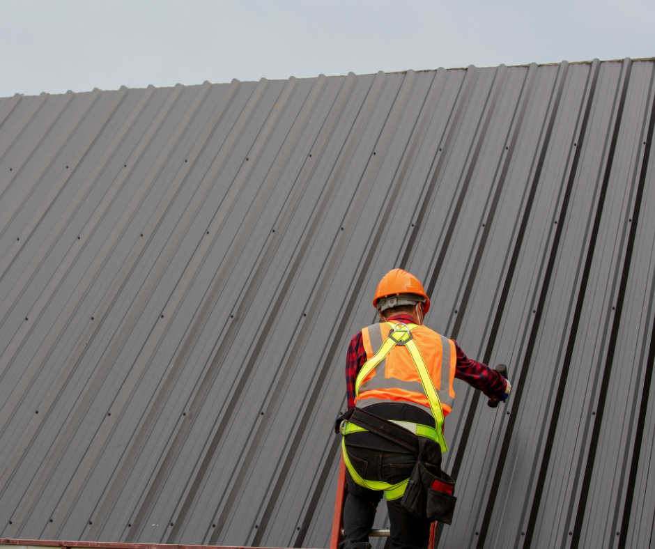 Construction worker on a metal roof, wearing safety gear and orange hardhat, working outdoors.