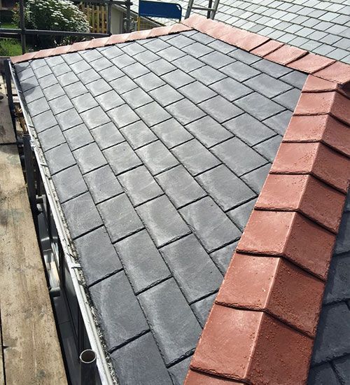 a slate roof with a red trim is being installed on a house .