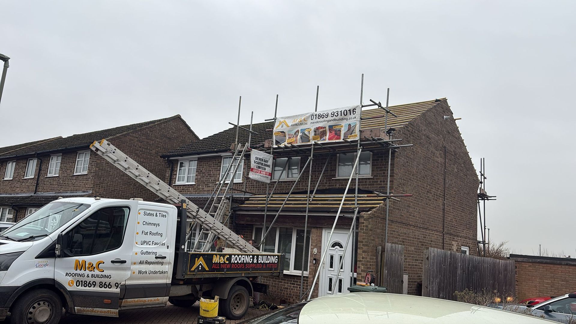 House under construction with scaffolding, a banner, and a work van parked in front.