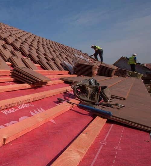 two men are working on a roof with a red roofing material