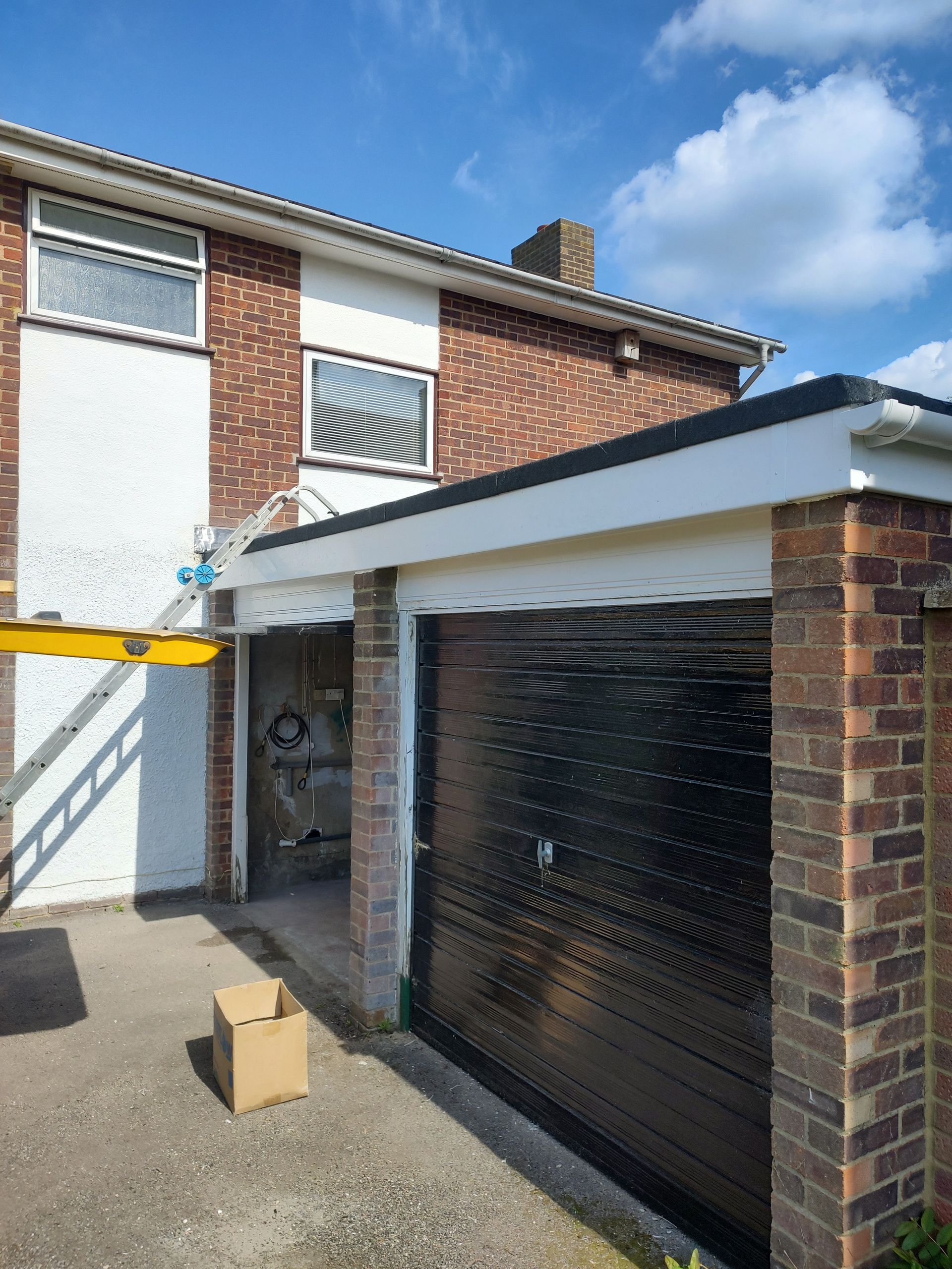 A two-story brick house with a garage featuring a closed black door and an open bay next to it, with a ladder propped up.