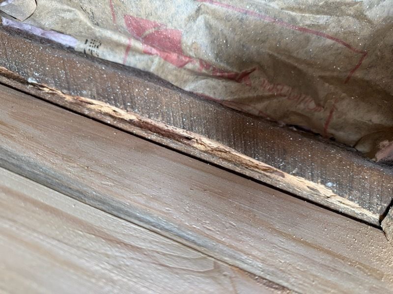 Wood trim with a damaged, discolored section, possibly water damage. Above is insulation.