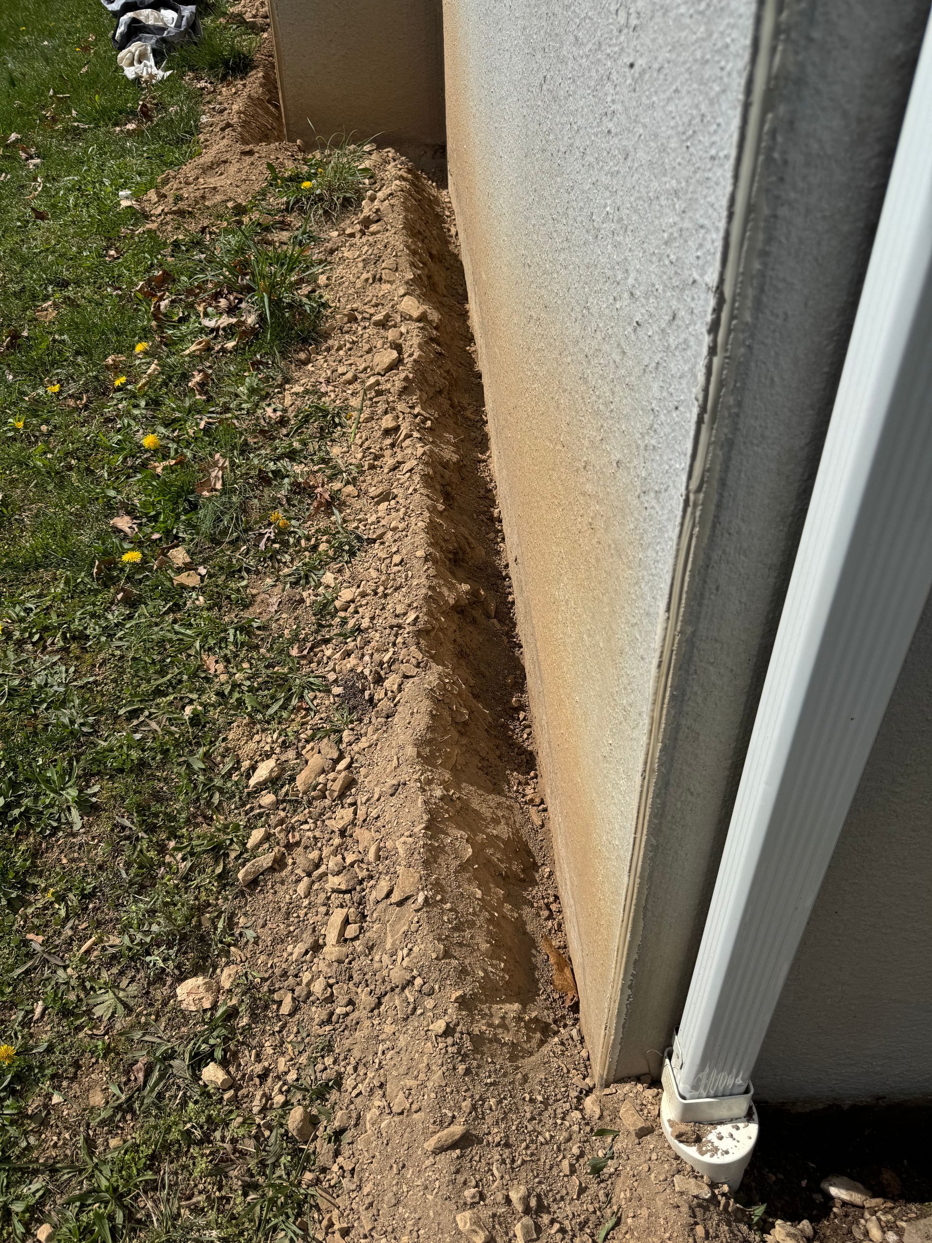 A trench dug along a concrete wall, next to a grassy area.
