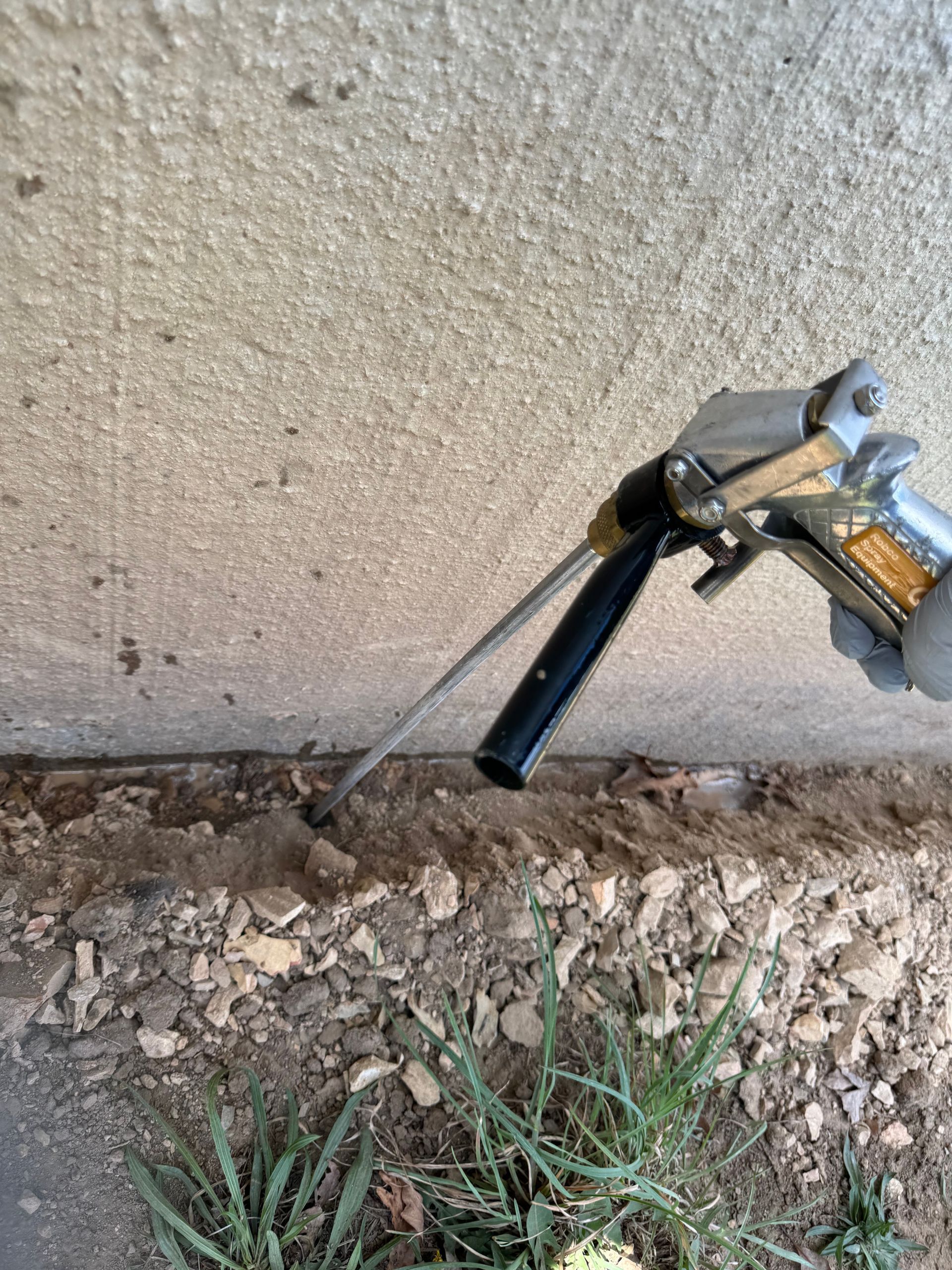 Hand spraying foam sealant into gap between concrete wall and ground.