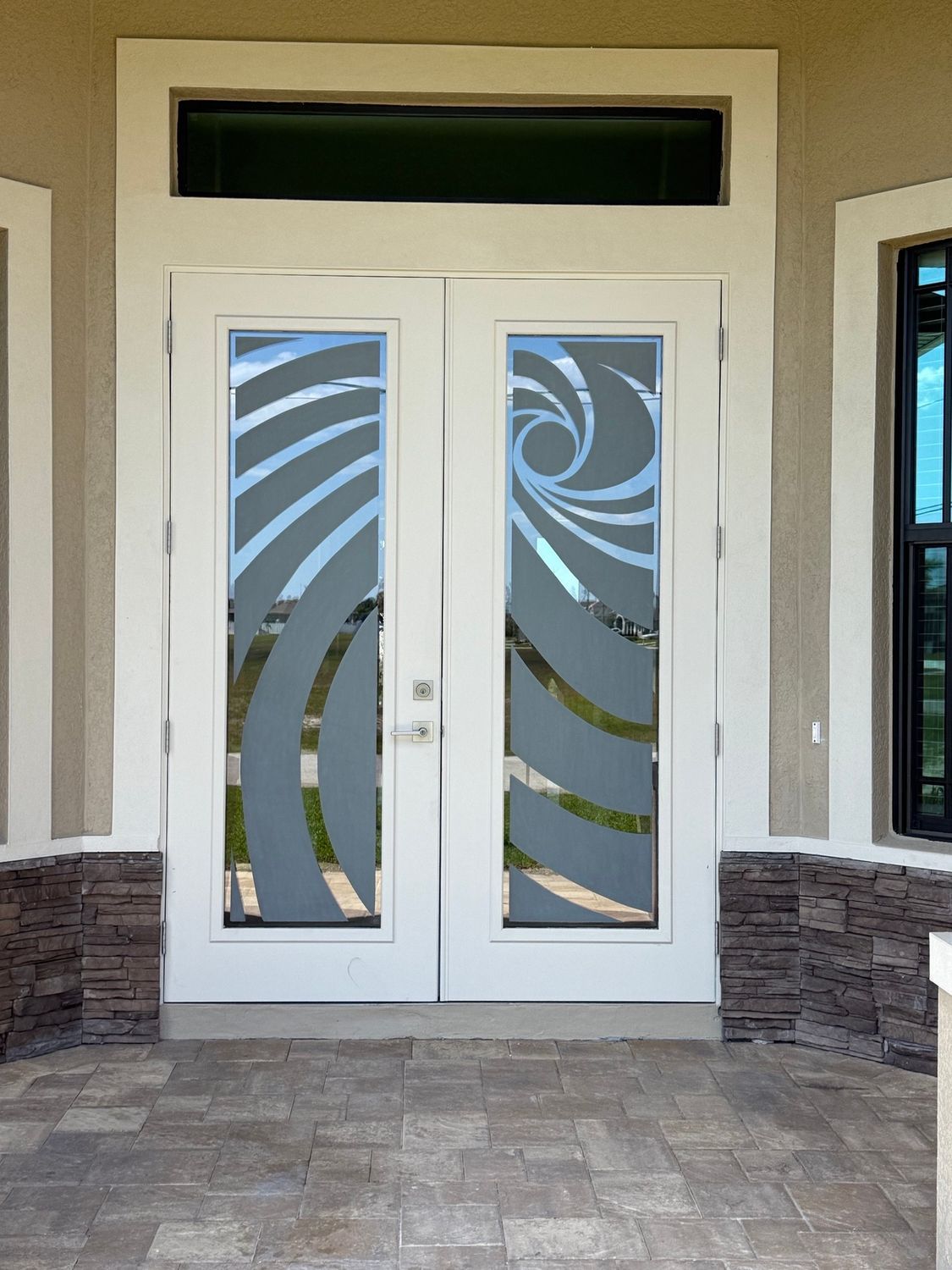 Double white front doors with frosted swirl designs, beige exterior, stone accents.