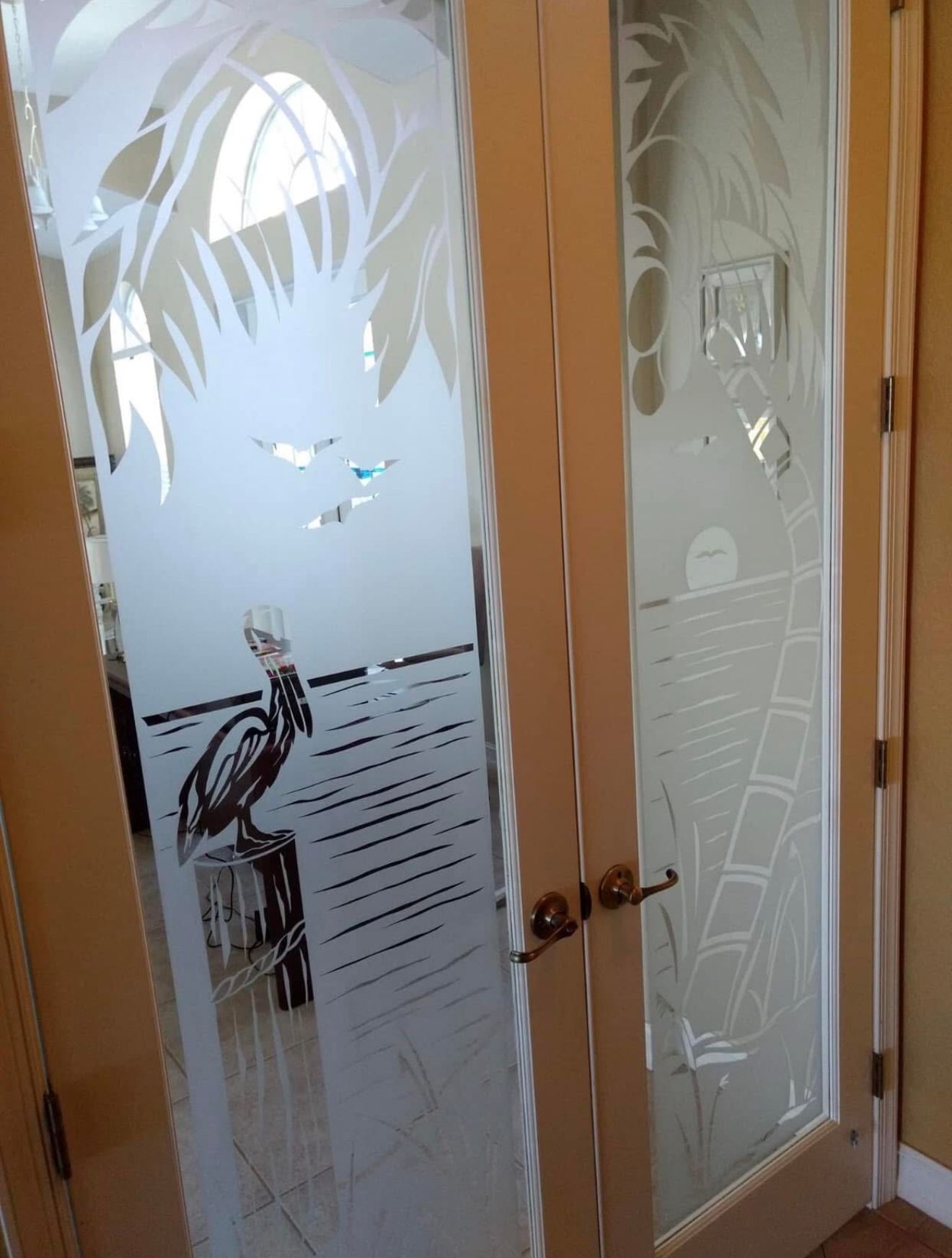 Etched glass French doors with coastal scene: pelican, birds, and stylized palm tree.