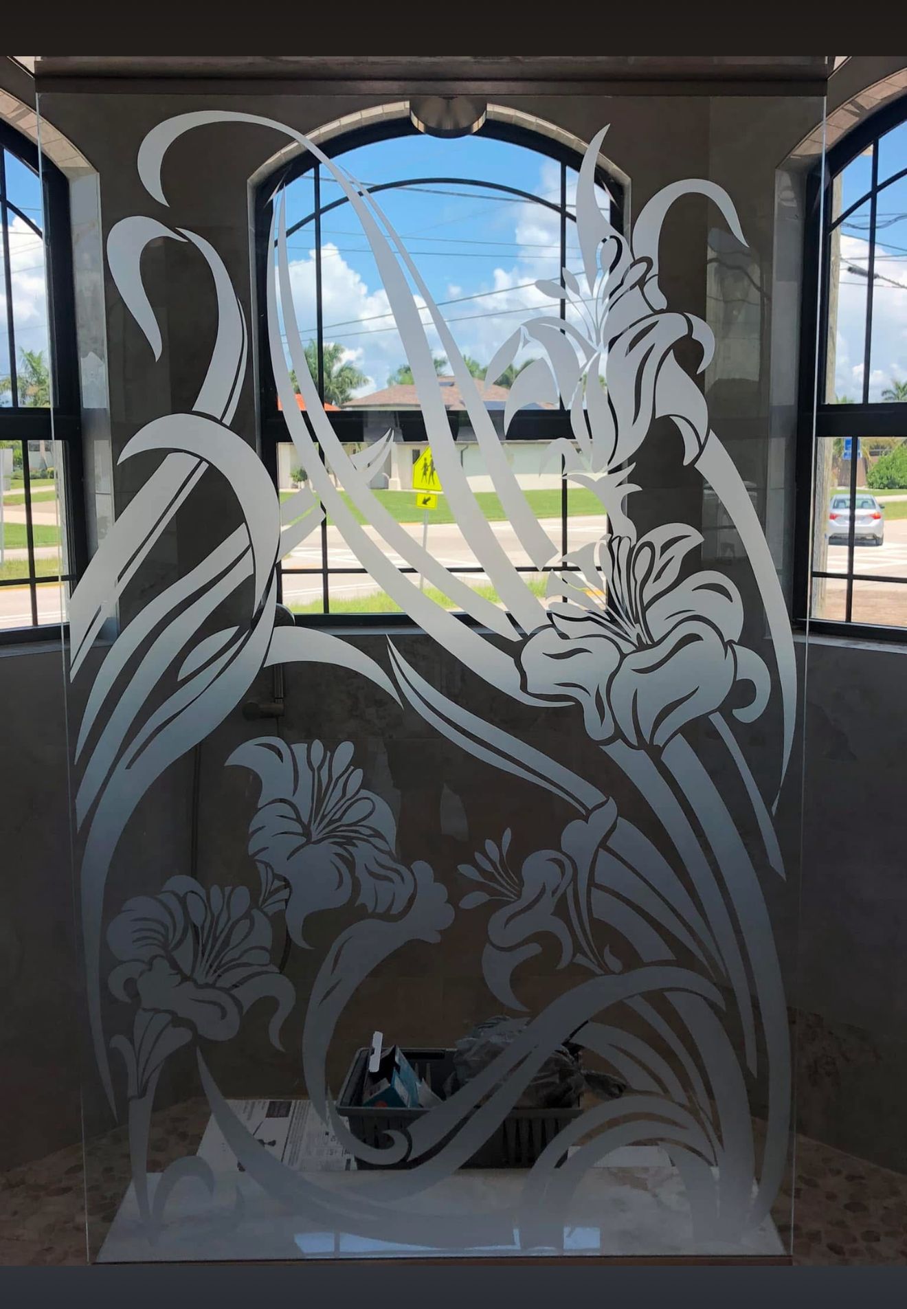 Frosted glass panel with floral design in front of a window with a bright sky.