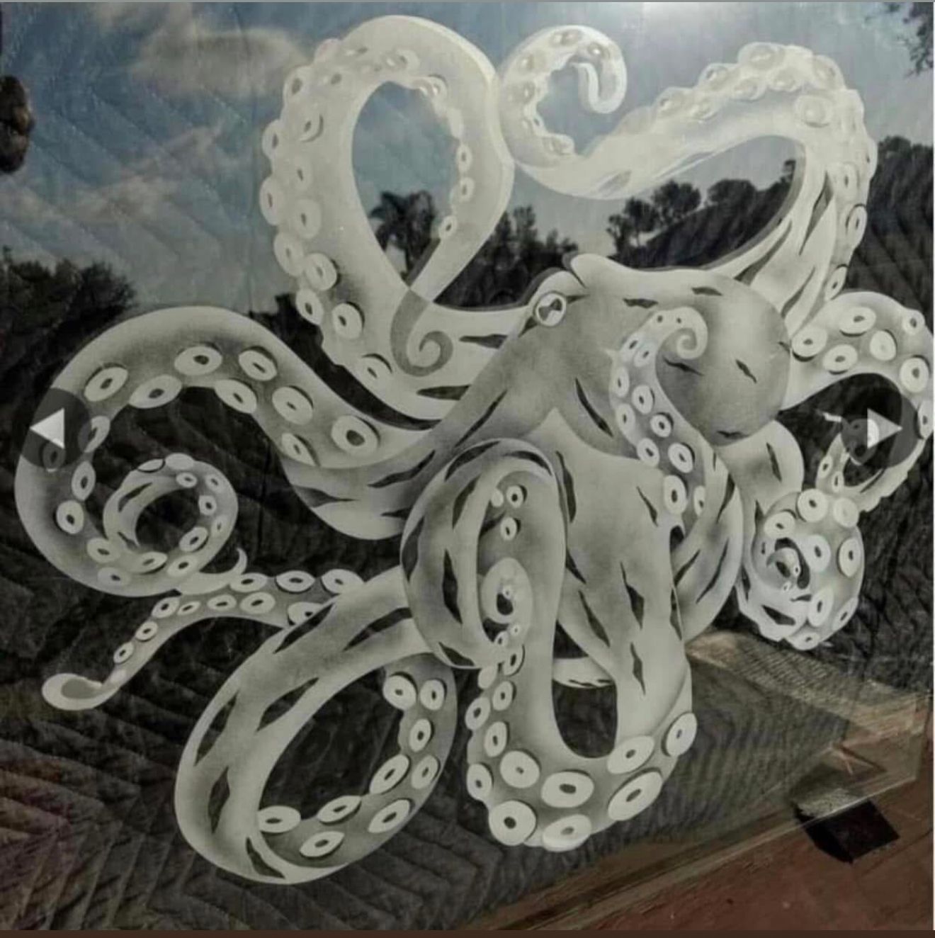 Gray octopus with swirling tentacles, over a landscape of trees and stone.
