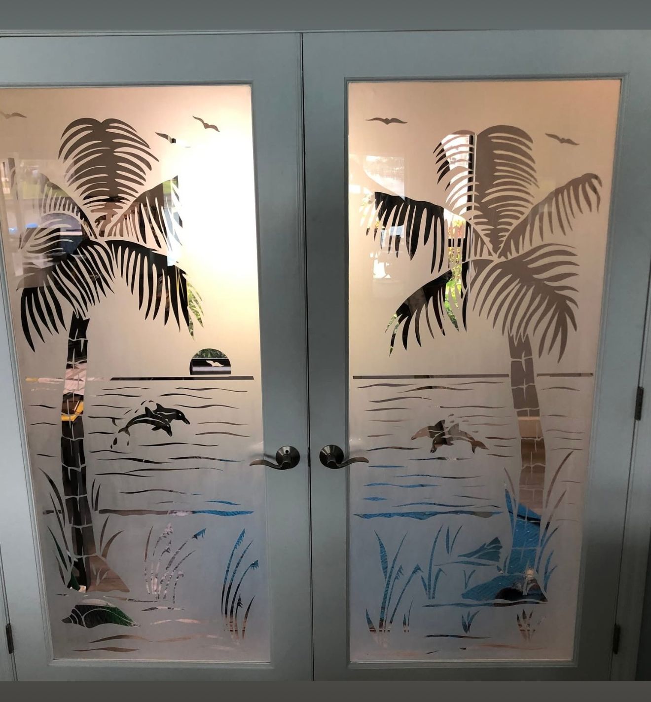 Frosted glass doors with etched palm trees, dolphins, and a sunset scene.