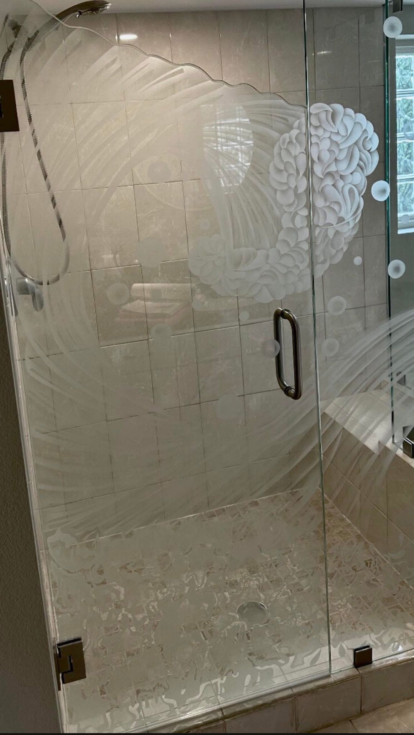 Shower door covered in soap scum, with a floral design, inside a tiled shower.