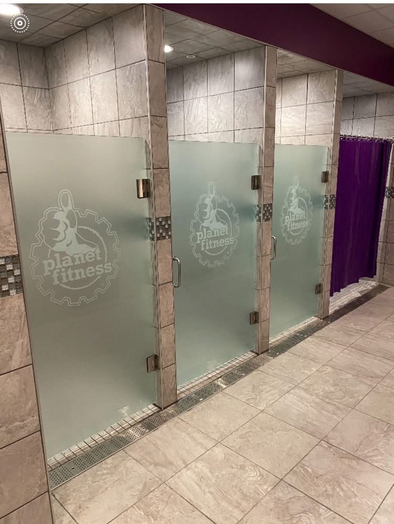 Planet Fitness gym shower stalls with frosted glass doors and purple curtain.