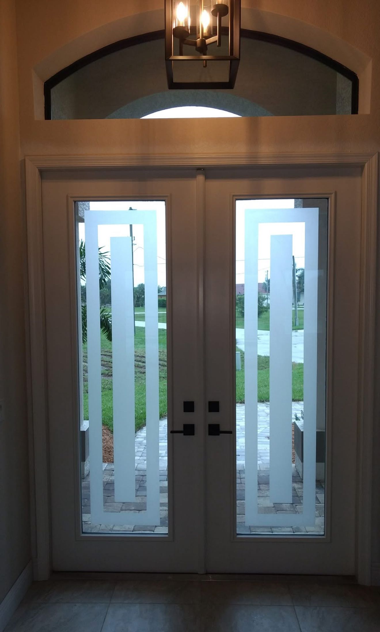 Double white doors with etched glass panels and a geometric design, under an arched window.