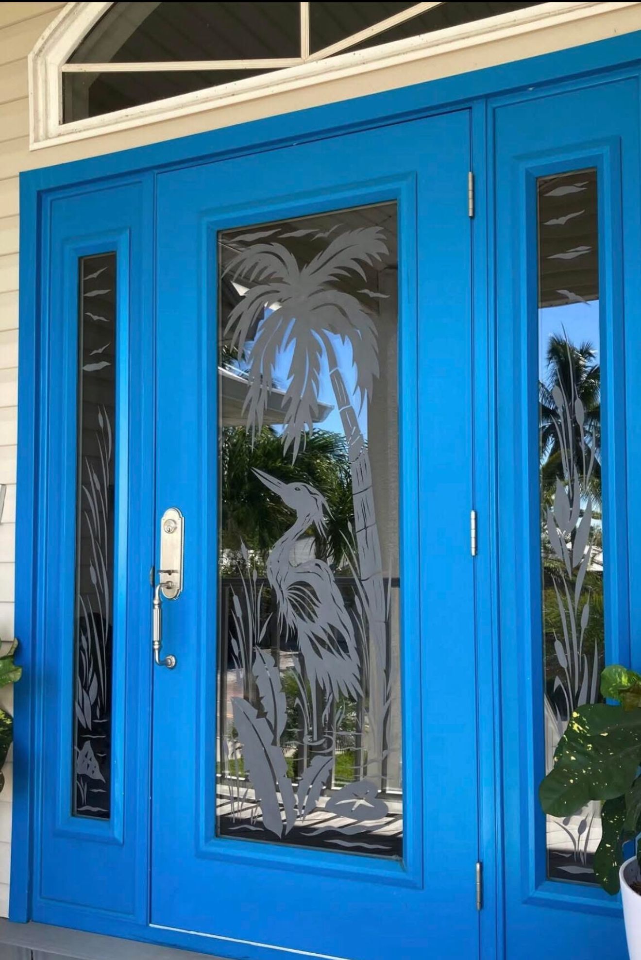Blue double doors with etched glass panels showing a heron and palm trees.