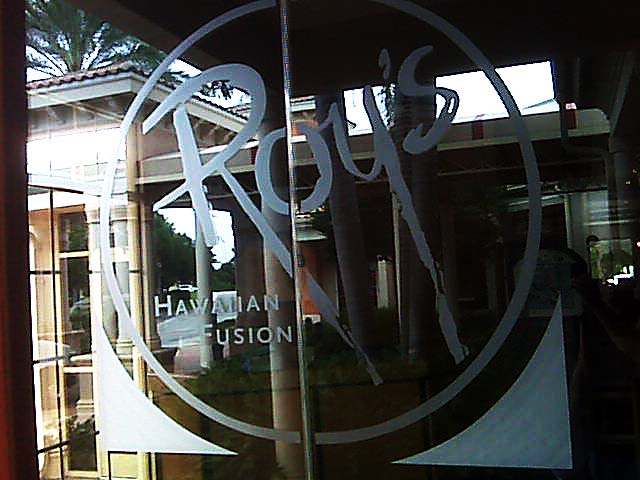 Roy's Hawaiian Fusion restaurant door with etched logo and text against a background of a building and palm trees.