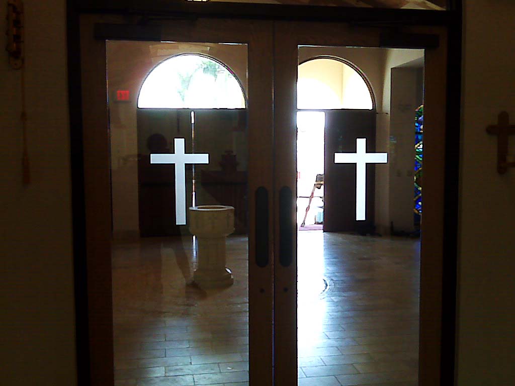 Wooden double doors with white cross decals, leading into a church interior with bright light.