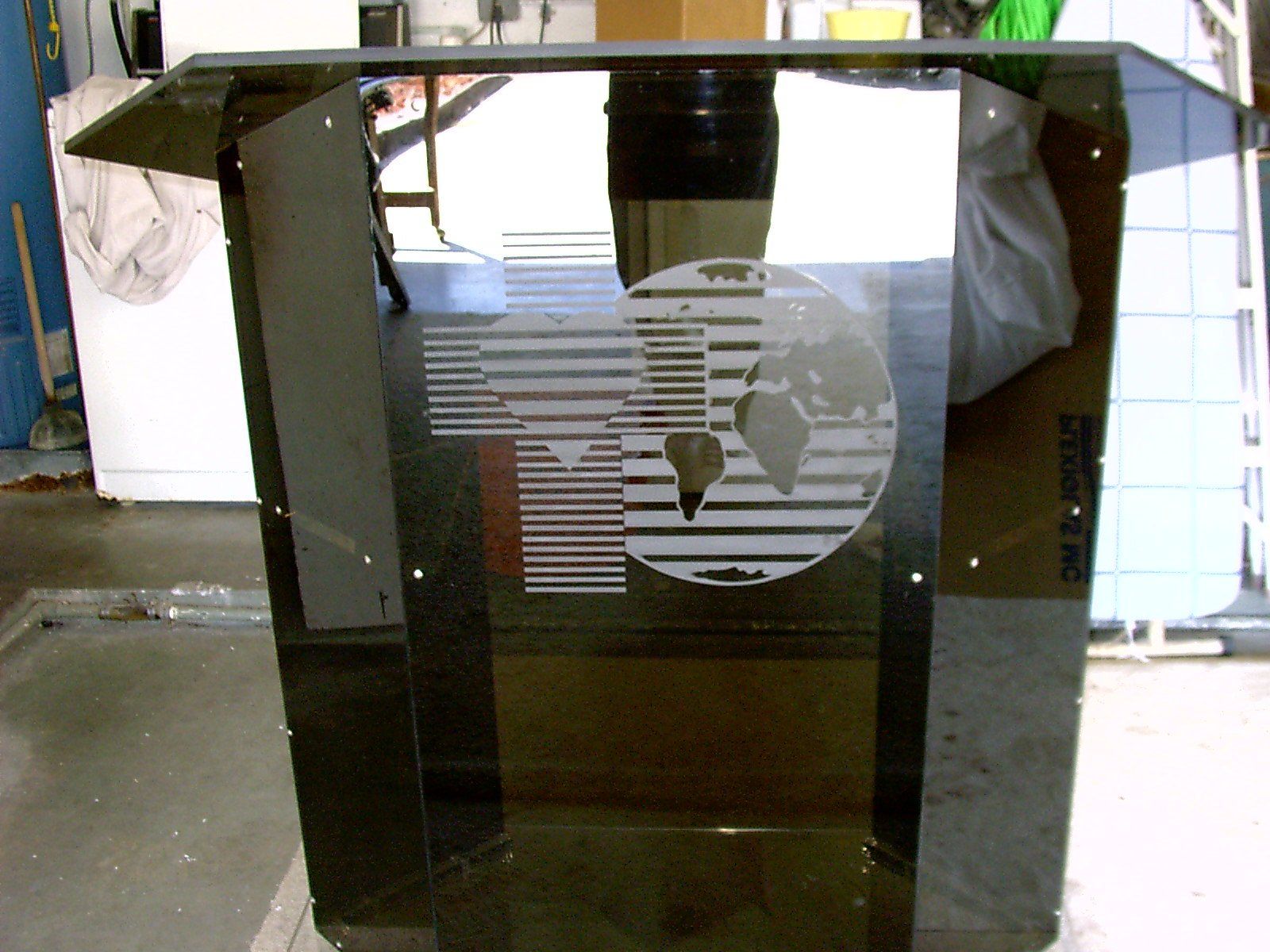 Dark podium with etched globe and logo, in a workshop setting.