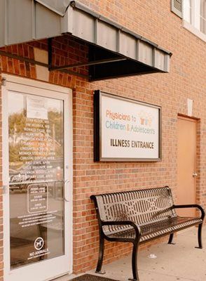 Exterior of medical clinic with brick facade, awning, entrance, sign, and bench.