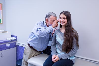 Doctor examining a patient's ear with an otoscope in a medical office.