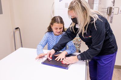 Woman in mask aligns a child's hand on an X-ray plate at a medical office.