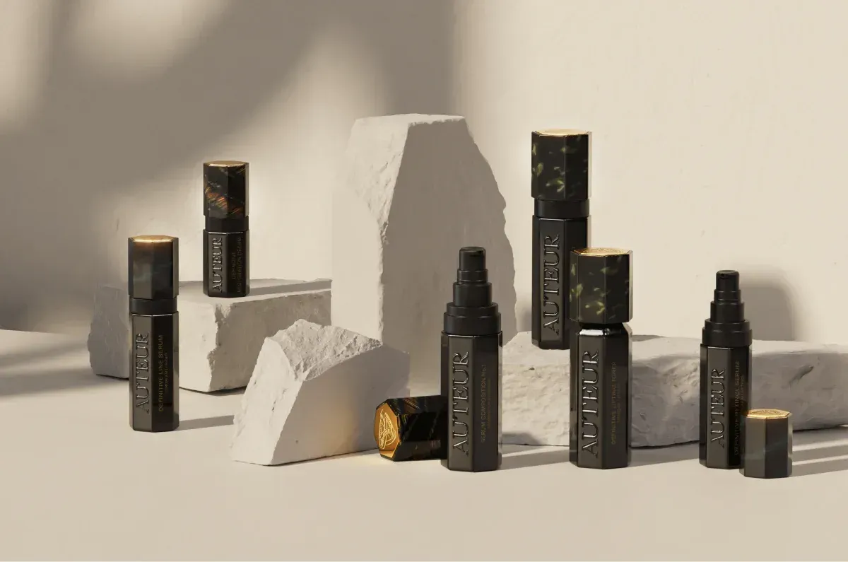 Assortment of black cosmetic containers with gold accents, displayed on and around white stone blocks.