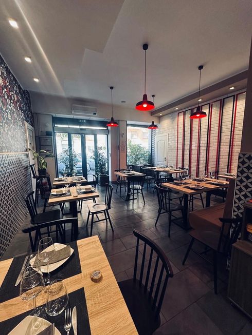 L'interno vuoto e moderno di un ristorante, con tavoli in legno, sedie nere e lampade a sospensione rosse su uno sfondo di mattoni bianchi.