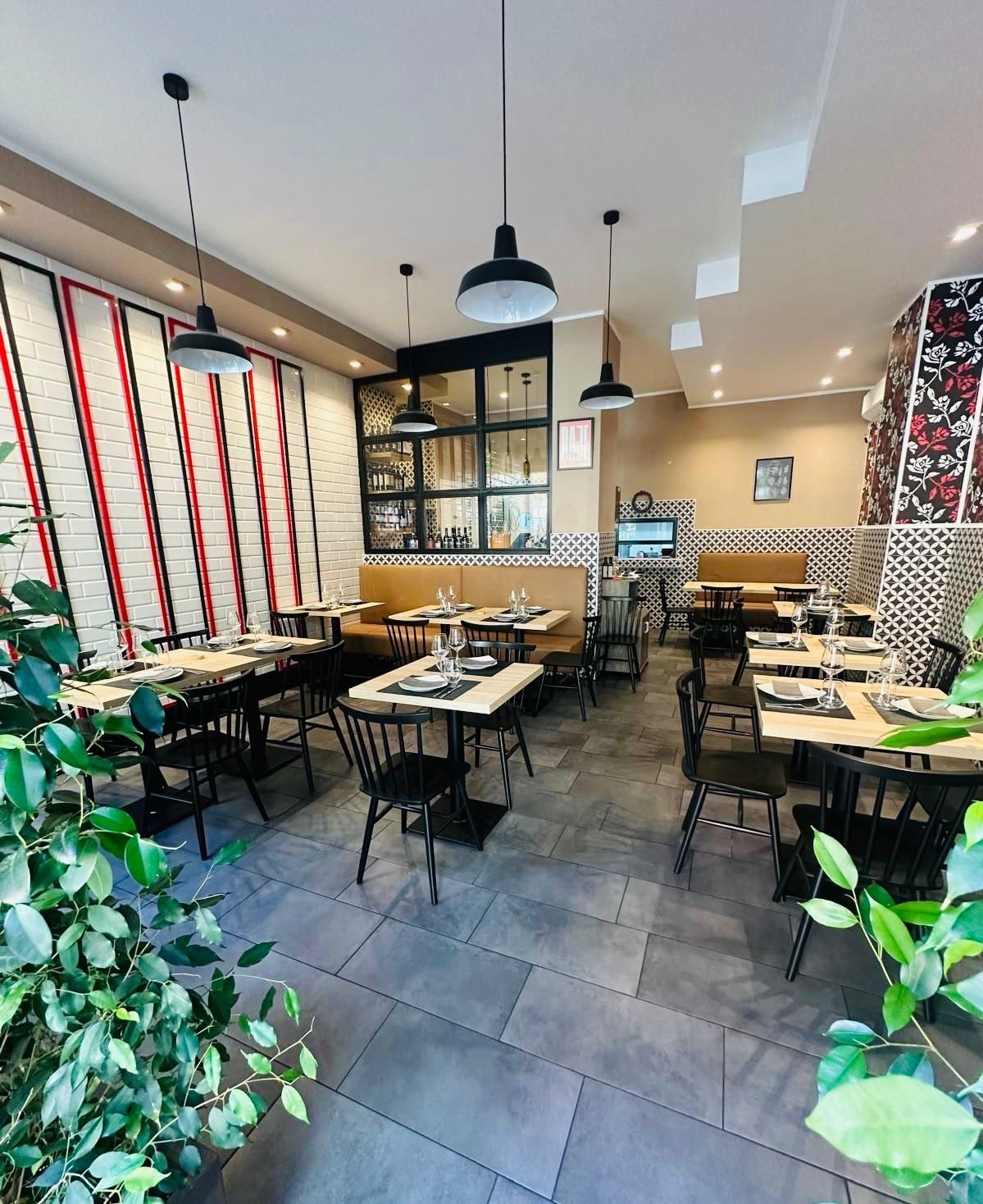 Una sala da pranzo accogliente, arredata con tavoli scuri, sedie nere, lampade a sospensione moderne e carta da parati a motivi geometrici.