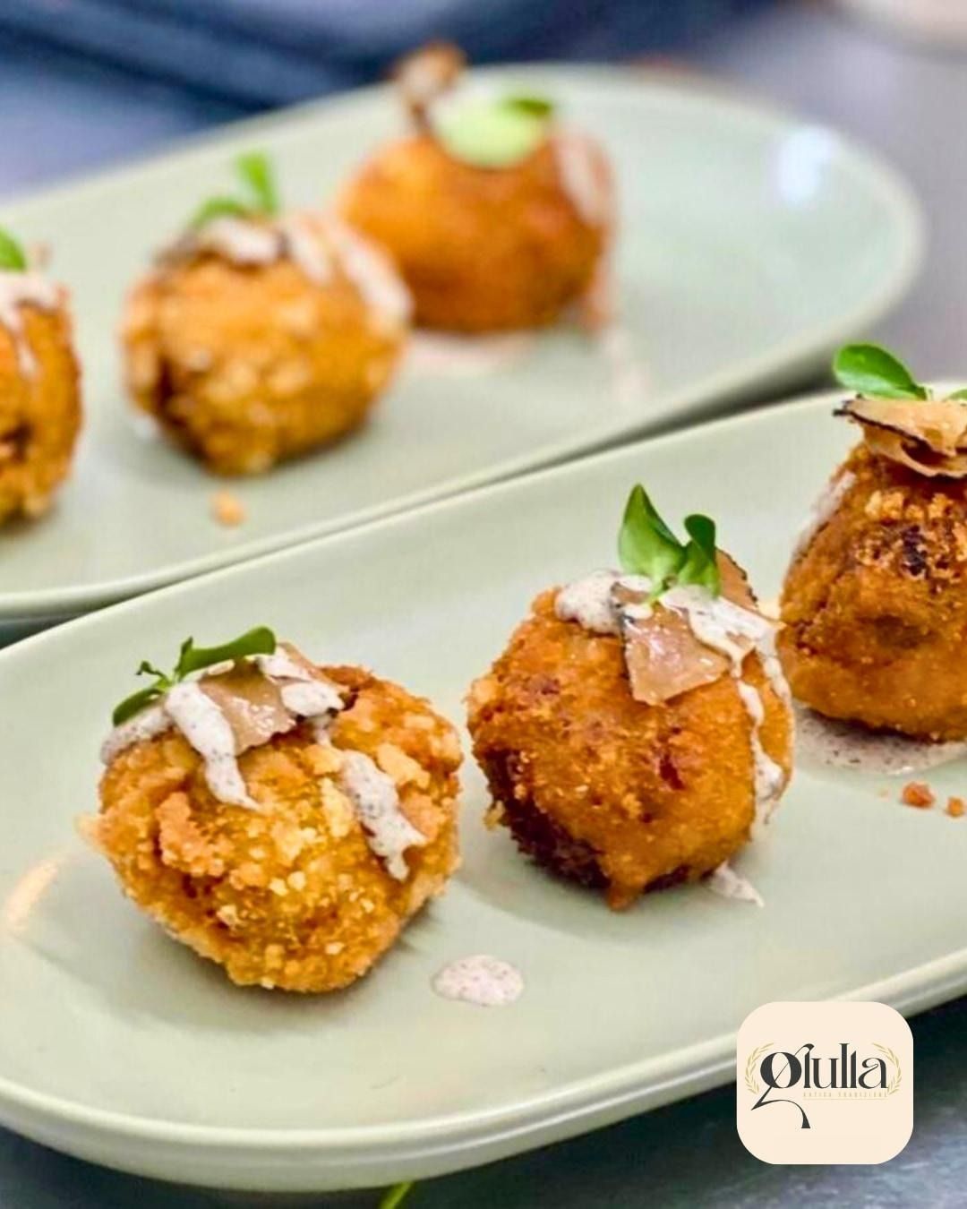 Palline da antipasto croccanti e dorate, guarnite con salsa alla panna ed erbe aromatiche, servite su piatti rettangolari verde chiaro.