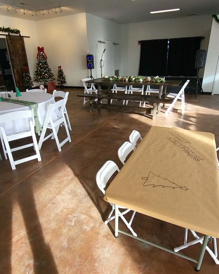 Event space decorated for the holidays; tables with white chairs, Christmas trees, microphones, and speakers.