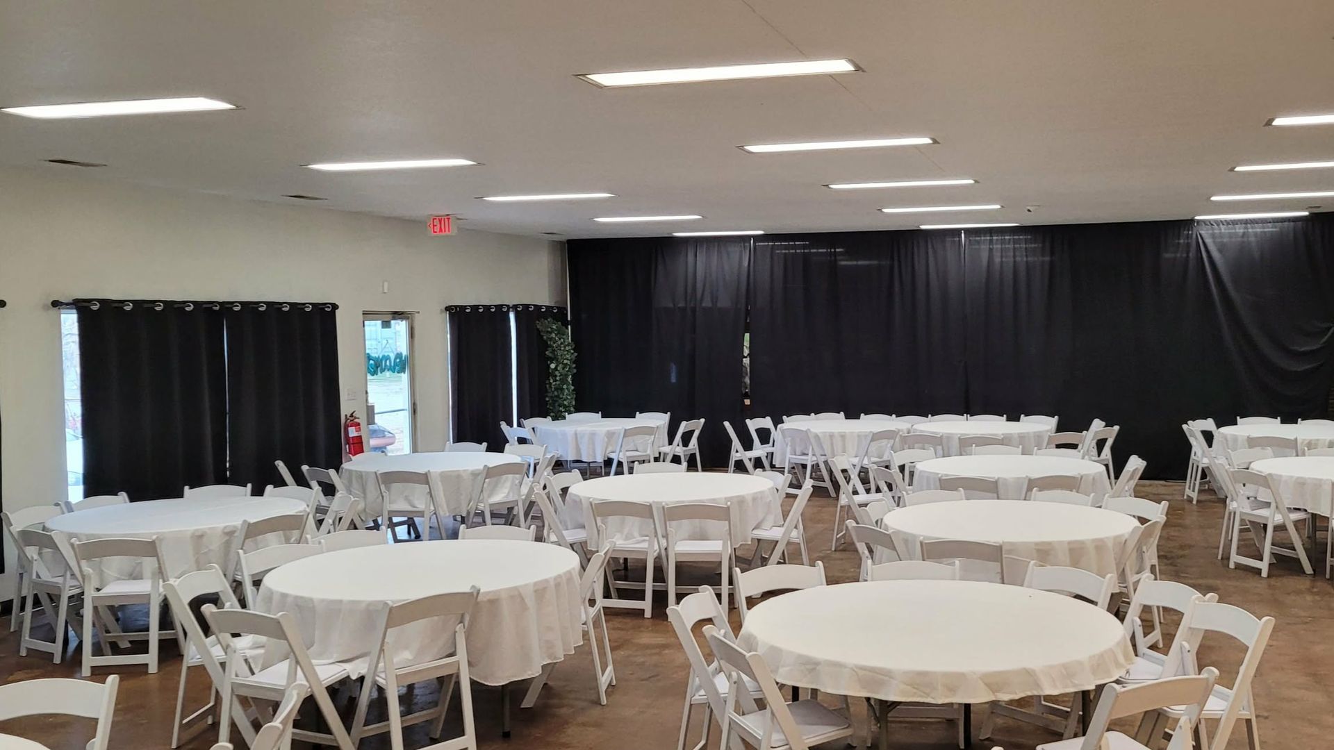 Empty event hall with round tables covered in white linens, white chairs, and black curtains.