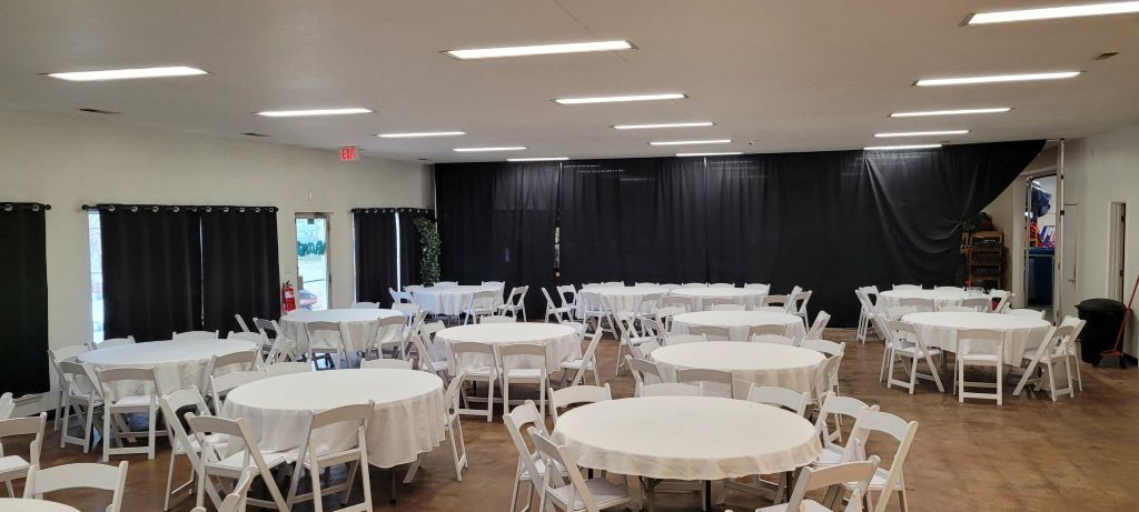 A large room with round tables, white chairs, and black curtains.
