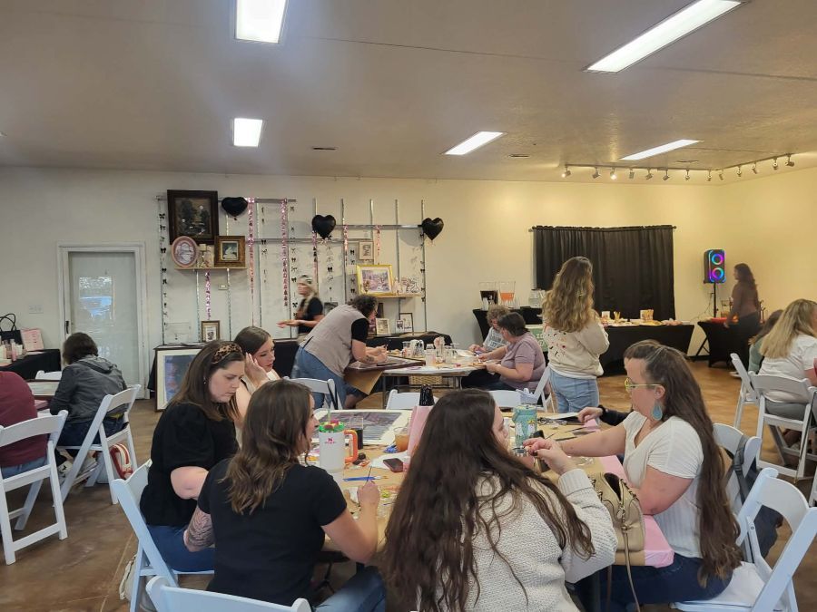 People gathered at tables in a brightly lit room, likely a craft event.