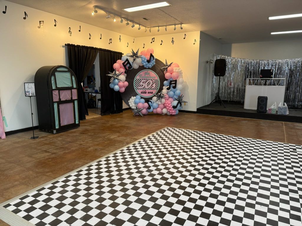 Party space with a black and white checkerboard dance floor, jukebox, and balloon arch.