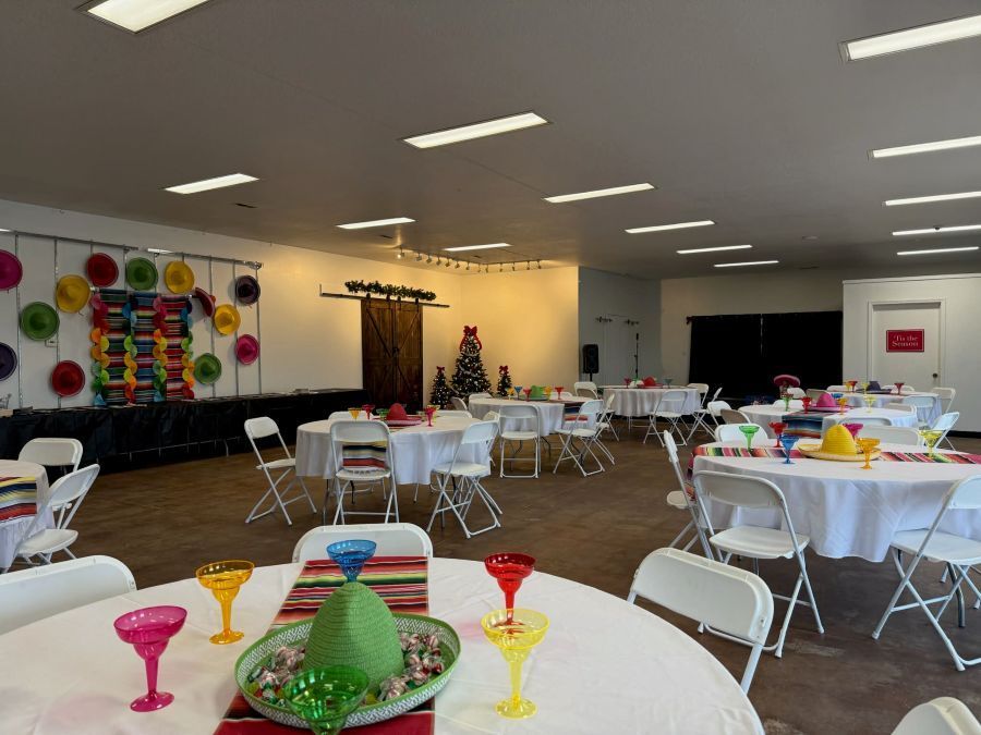 Event space with round tables, white chairs, and festive decorations, including sombreros.