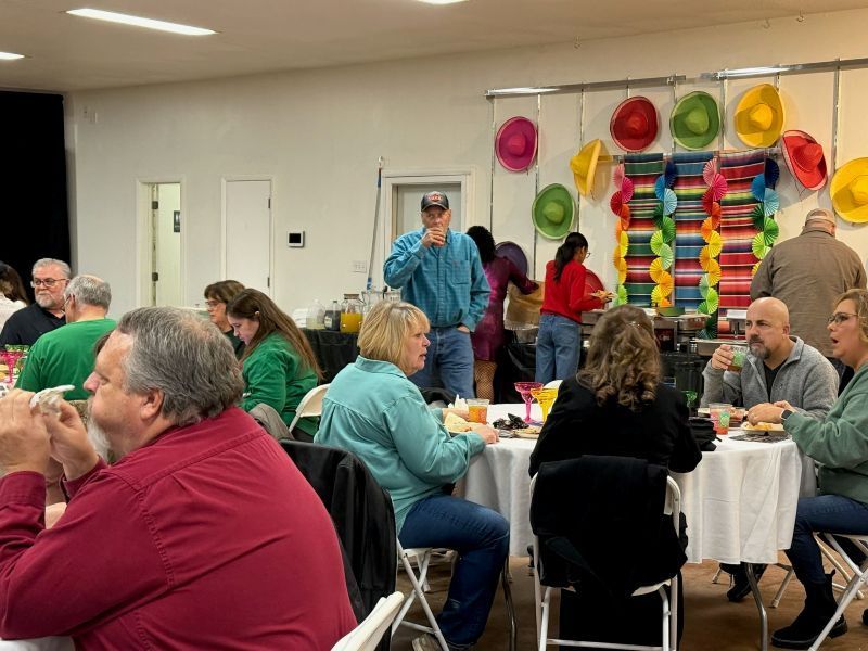 People at a party eating and socializing, with colorful decorations including sombreros.