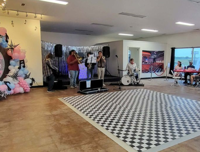 Band performing on astage area inside a building, with a silver backdrop and decorations.